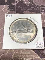 Reverse side of the 1937 Canadian silver 1 dollar coin showing a voyageur and Indigenous person in a canoe with inscriptions and date.