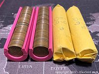 Two pink plastic rollers filled with Canadian 1 cent coins and two yellow paper coin rolls on a map-themed surface.