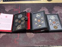 Three presentation coin sets in fold-out cases showing multiple Canadian coins including double dollars and standard denominations.