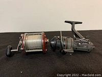 Two fishing reels placed side by side on a flat surface, showing general condition and size comparison.