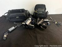 Photo showing both camcorders, power cords, battery packs, and two different soft carrying cases on black fabric surface