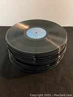 Stack of over 25 black vinyl LP records showing reflective surfaces and blue center label