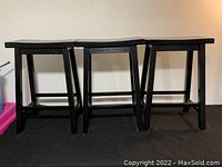 Three small black wooden bar stools placed side by side, showing front and top views.