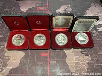 Four silver Canadian dollar coins in black display cases with red interiors, accompanied by informational cards for some coins.
