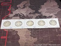 Five Canadian 50 cent coins dated 1961 to 1965 displayed on a world map surface in their white cardboard holders.