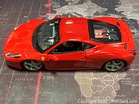 Side view of red 1/24 scale Ferrari 458 Italia die cast model car on world map background, showing details of doors, wheels and body shape.