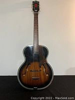 Full front view of guitar showing archtop body, sunburst finish, f-holes and leather strap