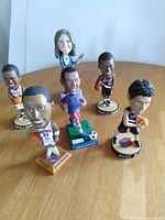 Six bobblehead figurines arranged on table: Melissa Etheridge with guitar; basketball players Shawn Marion, Martell Webster, Sebastian Telfair, RAEF; and baseball player Carlos Zambrano.