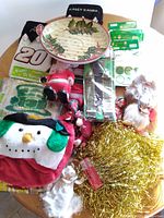 Photo of assorted Christmas and St. Patrick's Day decorations on a wooden table including a snowman hat, Santa figurines, angel figure, gold tinsel, and holiday plates and stickers.