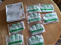 Two large boxes and multiple individual bags of disposable plastic gloves arranged on a wooden table.