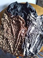 Three tops laid flat on table: dark gray pullover, leopard print top, black and white patterned top