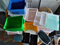 Photo showing a collection of plastic trays and containers of various colors and sizes arranged on a table.