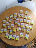 Top-down photo of 38 individual magnetic eyeglass holders in plastic packaging spread in a circle on a wooden round table.