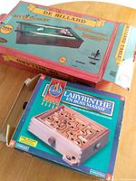 Photo of boxed tabletop billiard game and boxed solid wood labyrinth game on a wooden surface.