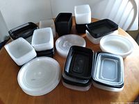 Array of approximately 16 plastic food storage containers with lids, placed on a round wooden table, showing a variety of sizes and colors.