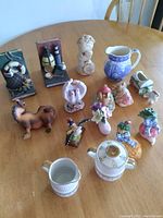 Image showing all collectible ceramic and pottery items laid on a wooden table including bookends, milk jug, cups, salt and pepper shakers and various figurines.