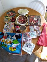 Photo showing all items from a top angle on the table including the wall hanger, plates, umbrella, napkins, puzzle, Santa figurine and plant holders, and cassettes.