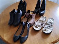 Photo of six pairs of women's shoes in sizes 7-7.5 displayed on a wooden table. Shoes include heels, boots, flats and sandals in black, brown, and beige.