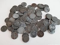 Multiple images showing a pile of approximately 100 U.S. Lincoln wheat pennies spread on a white surface. Coins show darkened, silver/gray toned surfaces instead of typical copper coloring.
