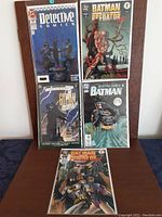Five Batman related comics arranged in front of a wooden backdrop on a table. Covers shown clearly with artwork from 1990s DC comics.