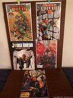Photo showing all five Judge Dredd comics arranged in a grid. Front covers visible illustrating different scenes and characters from the 1990s comic series.