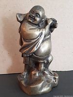 Front view of the bronze Buddha statue showing smiling face, robe details, and rounded base.