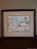 Framed watercolour painting depicting Middle East architectural scene with buildings and palm trees in light earthy tones.
