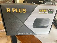 Closed retail box of R Plus OTT Smart Box with branding and feature icons 4K Ultra HD and H.265 HEVC