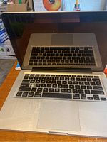 Front view of Apple MacBook Pro keyboard and screen, showing wear and black keys with silver casing.