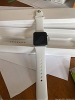 White sport band watch laid out on wooden surface showing front