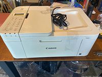 Image showing front and top view of white Canon PIXMA TR4522 printer on table with power cord placed on top.