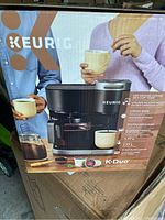 Front image of Keurig K-Duo coffee maker box showing people holding cups and product image with key features.