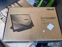Photo of the retail box for ASUS ZenScreen MB165B 15.6-inch portable monitor with product image and branding visible.