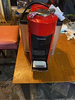 Red Nespresso Vertuo Evoluo coffee and espresso machine from front view on wooden table.