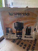 Photo of the front side of the box showing branding and model name Nespresso Vertuo Next by Breville with product image and capsule compatibility indications.