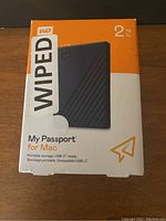 Front of the boxed WD My Passport for Mac 2TB portable external hard drive showing branding, capacity, and wiped sticker