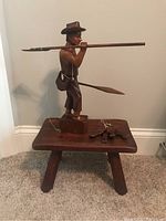 Full view of the wooden stool with the carved figurine and metal fish sign on top, showing size and condition.