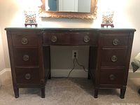 Full front view of the antique mahogany vanity showing all drawers and brass ring pull hardware, and glass top surface.