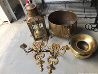Overall view showing the brass lantern, large bowl, smaller ring bowl, and wall sconces on concrete floor.