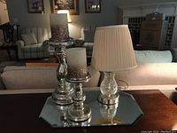 Photo capturing both mercury glass candle holders with decorative candles, placed on a mirrored tray in a living room setting.