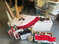 Lot of assorted Christmas decorations including vintage tree skirt, boxed ornaments, and glitter trees on a table