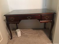 Full view of the cherry wood desk with glass top and three drawers underneath.