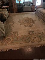 Full view of large rectangular floral area rug on hardwood floor in living room setting showing central oval medallion and light fringe on short side.