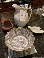 Photo showing all four ceramic items including two pitchers, floral bowl, and small leaf dish on a dark kitchen countertop.