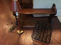 Wooden two-tier shelf with a small brown shade lamp and black metal mail holder on a wooden floor.