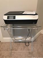 Front view of HP ENVY 5530 wireless printer on clear lucite stand with power cord visible.