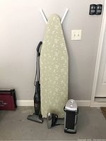 Photo showing the ironing board, handheld steamer, upright vacuum, and two remote controls hung on the wall