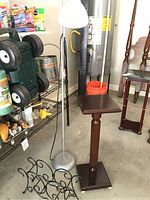 Floor lamp, wooden plant stand, and black iron magazine holder arranged together in garage setting.