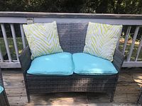 Outdoor patio loveseat with two blue seat cushions and two yellow-white patterned back cushions on a grey woven rattan frame.