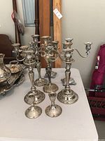 Wide view of silver plated candelabras and candlesticks depicting variety in sizes and ornate bases